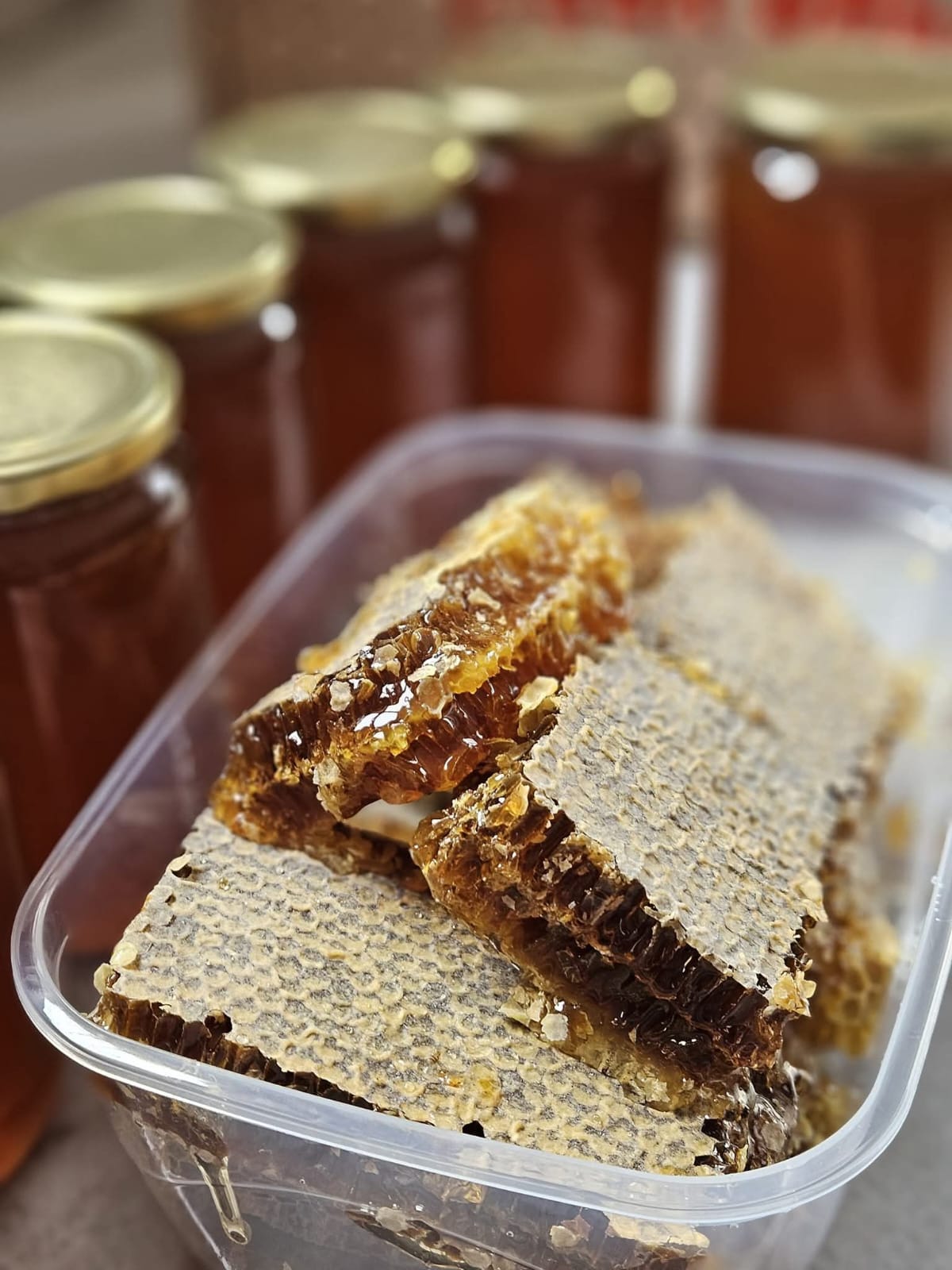 Cut comb honey pieces in a tub with honey jars behind